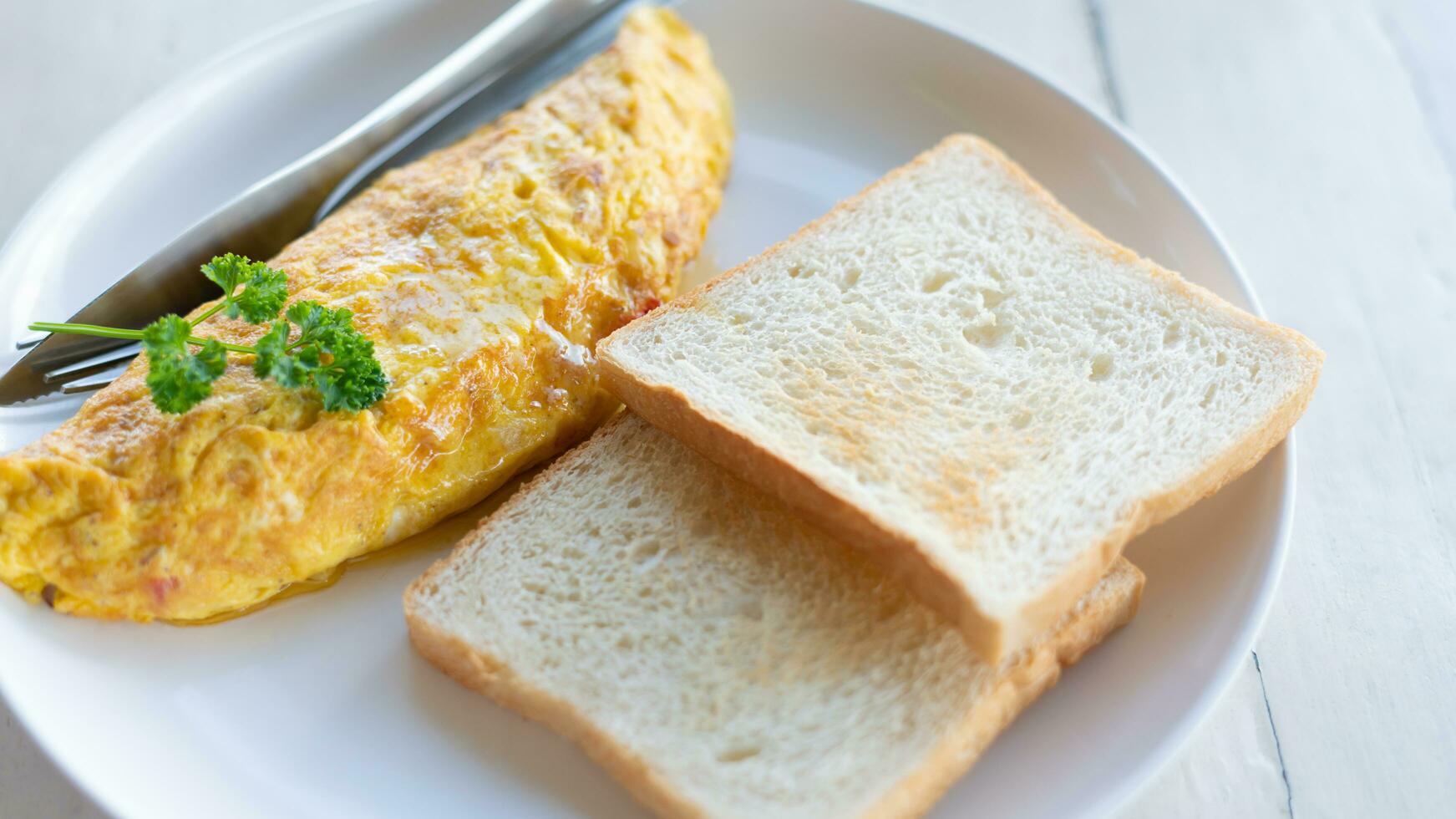 delicioso revuelto huevos en parte superior con perejil y un pan en un blanco plato en de madera mesa foto