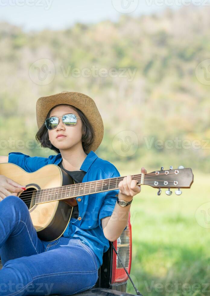 Woman wear hat and playing guitar on pickup truck photo
