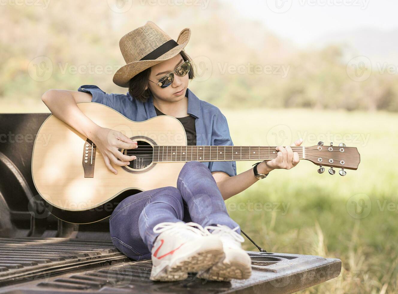 Woman wear hat and playing guitar on pickup truck photo