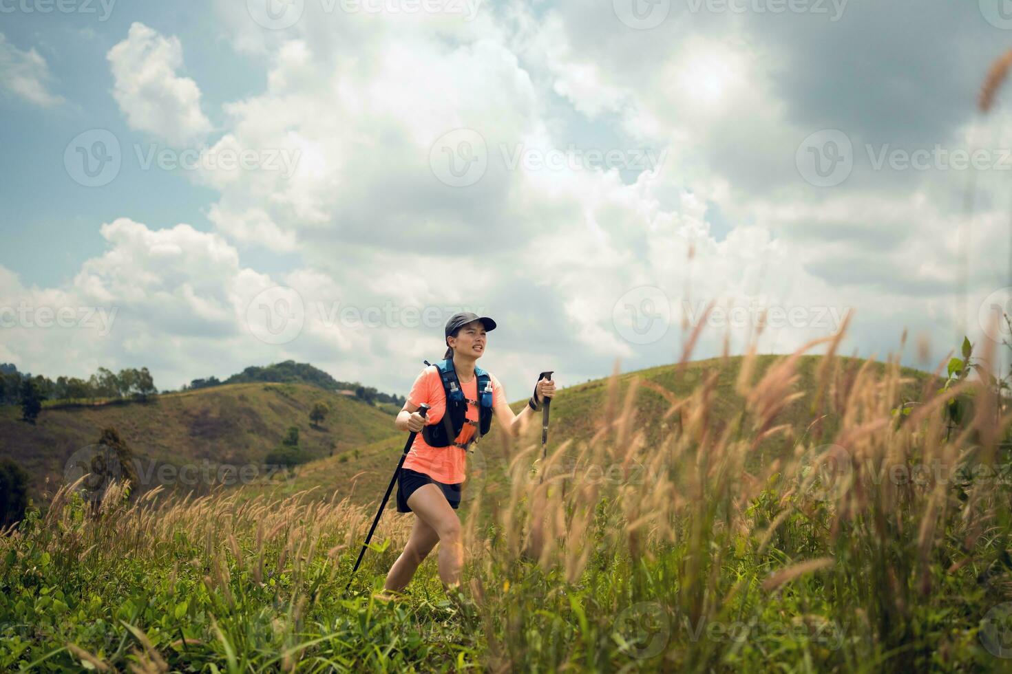 Young women active trail running across a meadow on a grassy trail high in the mountains in the afternoon with trekking pole photo