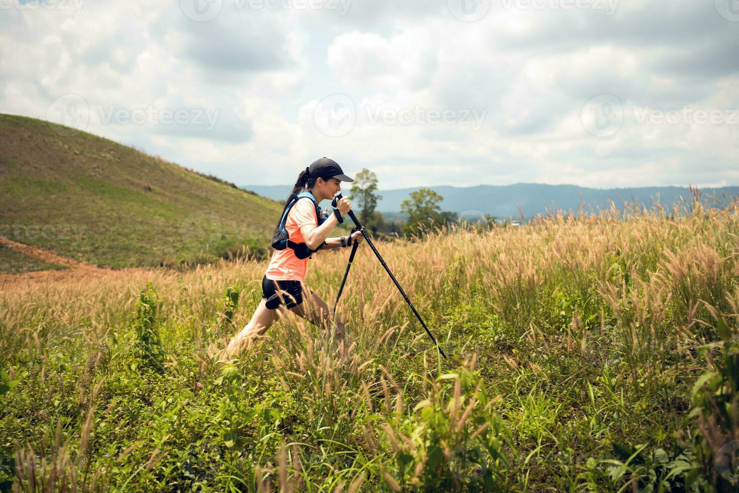 Young women active trail running across a meadow on a grassy trail high in the mountains in the afternoon with trekking pole photo