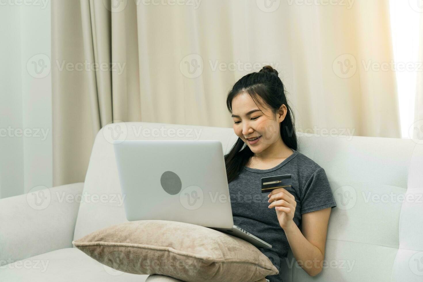Asian woman holding a credit card for online shopping while sitting on the couch while on vacation at home. photo
