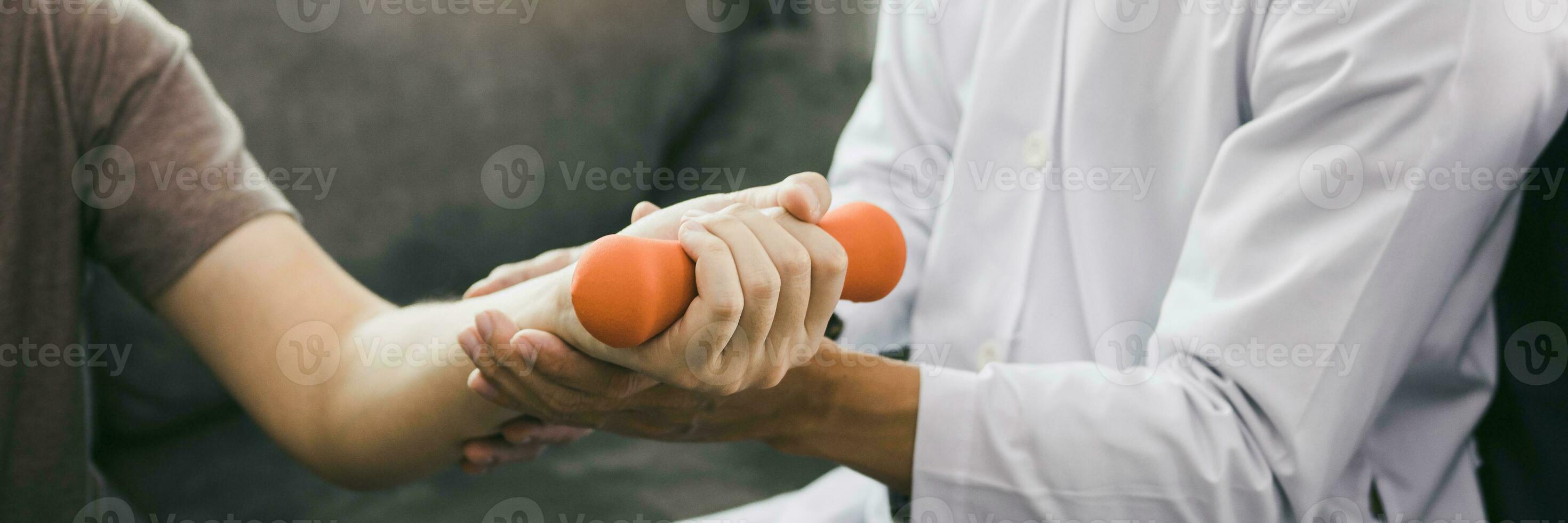 Asian physiotherapist helping a patient lifting dumbbells work through his recovery with weights in clinic room. photo