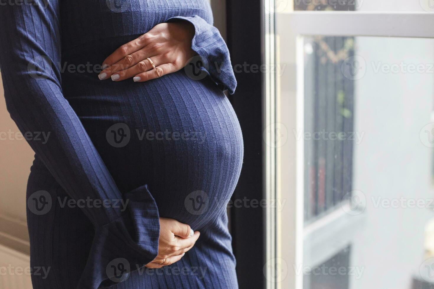 pregnant woman's belly closeup. hands hugging belly in blue background