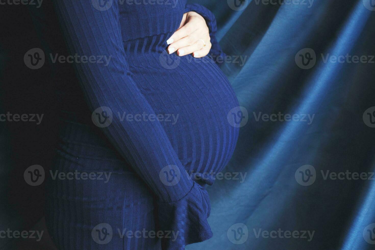 pregnant woman's belly closeup. hands hugging belly in blue background