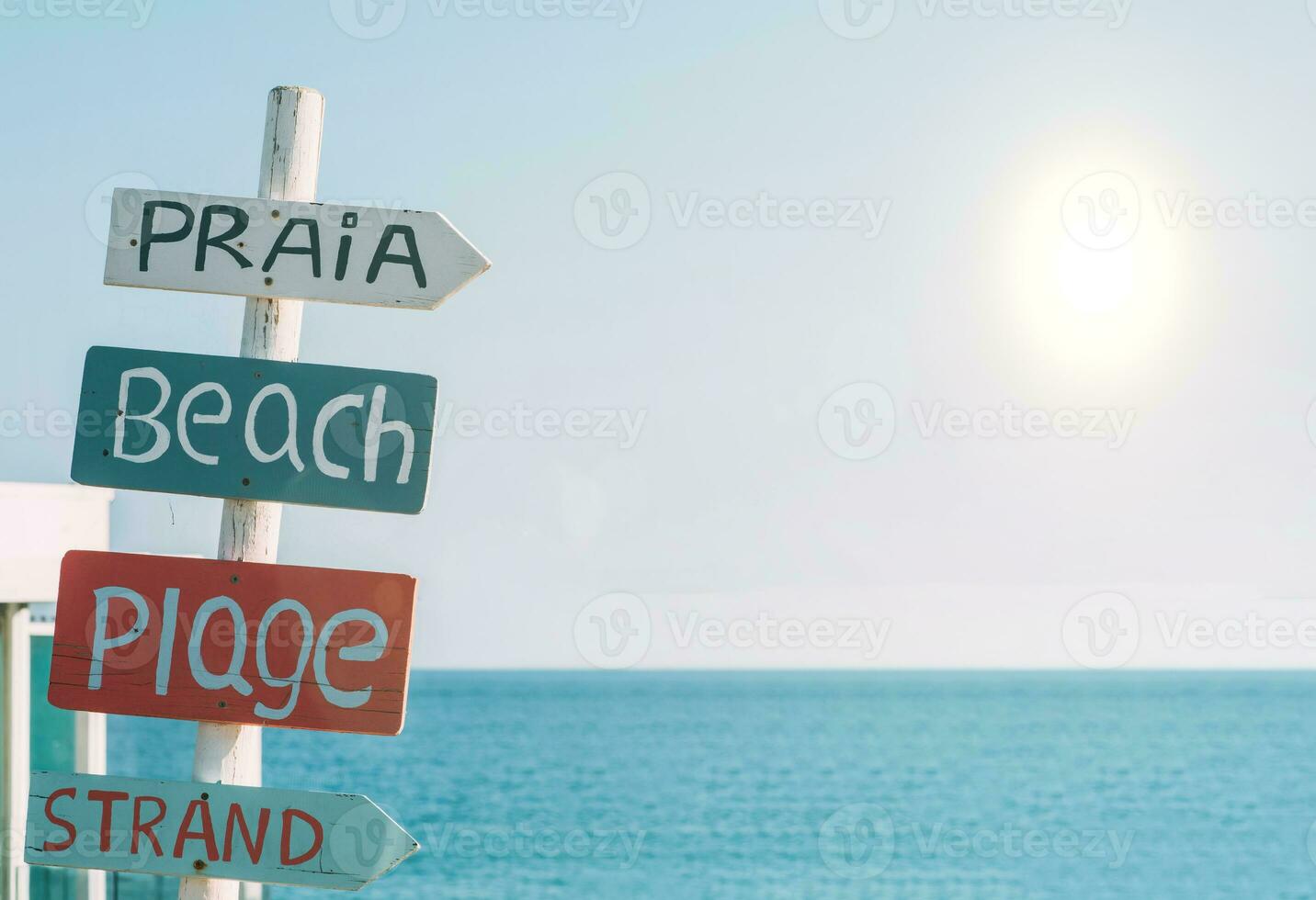 Sign on a beach in Algarve, Portugal translating beach in various languages including, Portuguese, English, French and Dutch with a giant sun flare visible photo