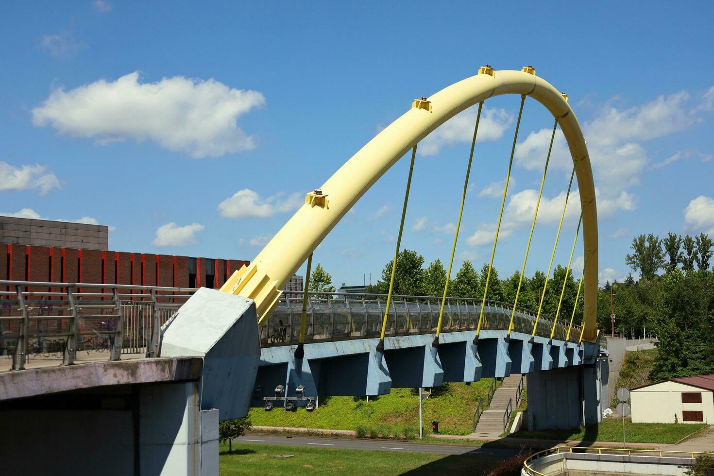 KATOWICE, POLAND, 2021 - Pedestrian bridge over Walentego Rozdzienskiego Alley in Katowice. Cose-up of the arch of the yellow footbridge. The car road passing underneath. Summer sunny day photo