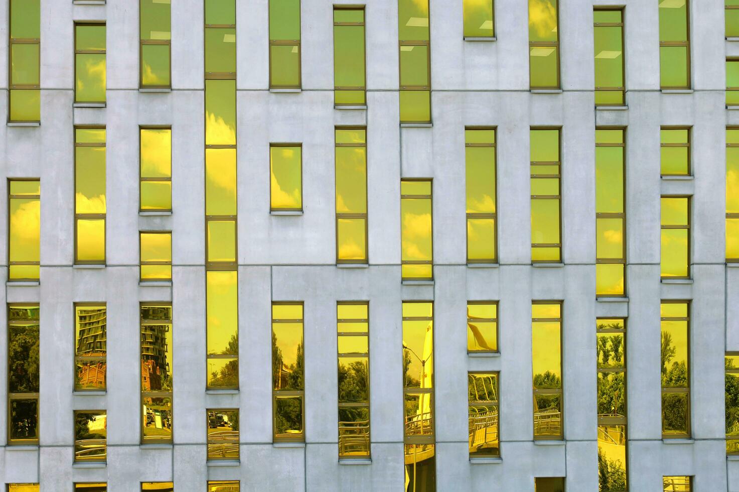 KATOWICE, POLAND, 2021 - Fragment of office building facade made of yellow toned glass and concrete constructions. Frontal view. Reflection of the sky and cityscape in the mirrored windows photo