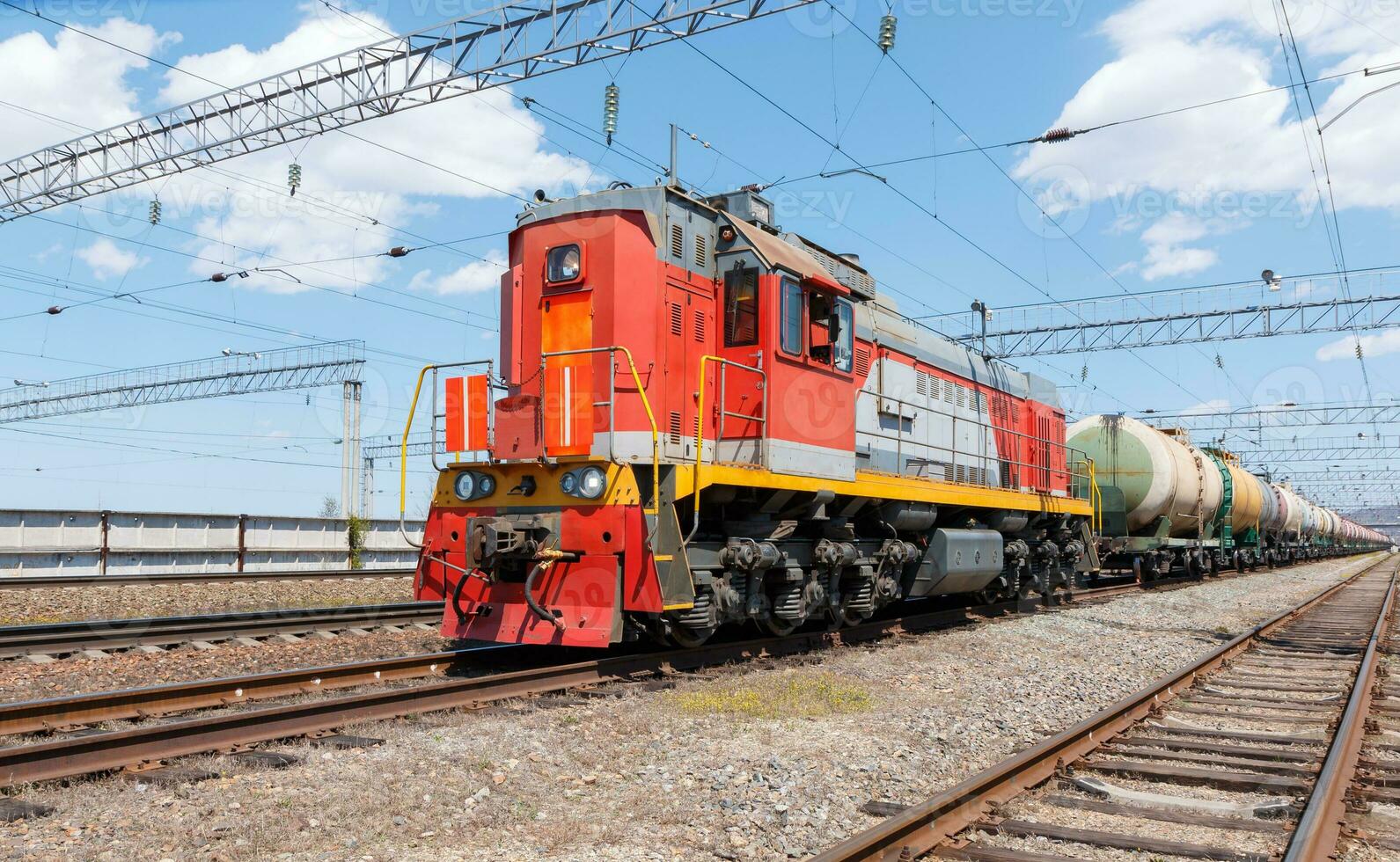Freight locomotive pulls train with fuel tanks against blue sky. photo