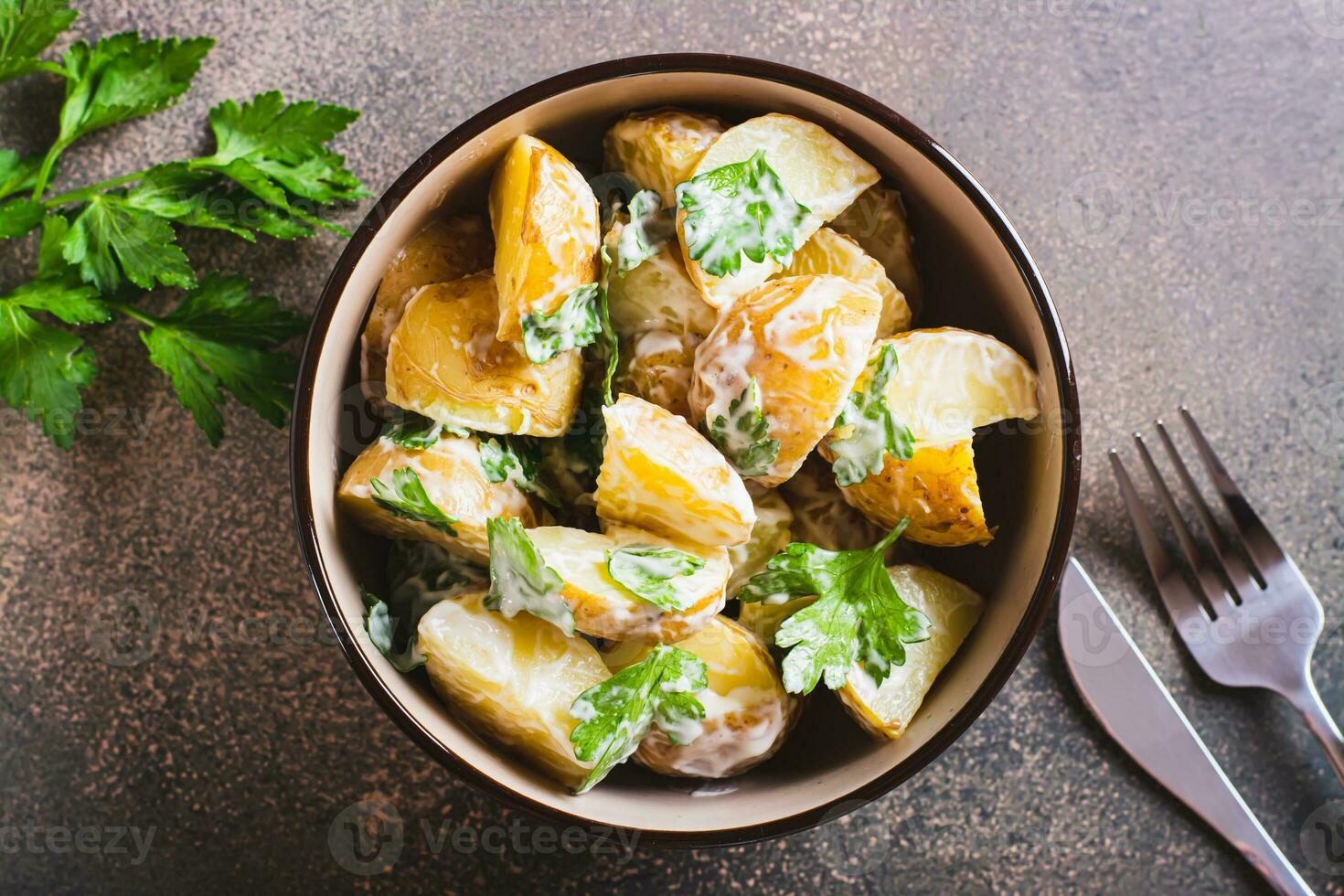 Close up of potato salad in a peel with parsley and mayonnaise in a bowl on the table top view photo