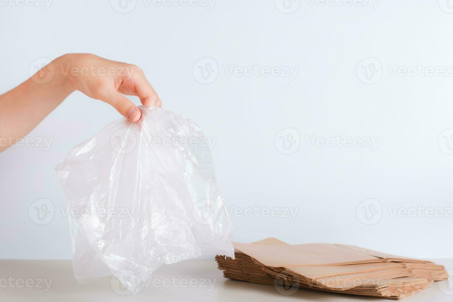 Hand with a disposable transparent bag and a stack of eco-friendly paper bags on the table photo