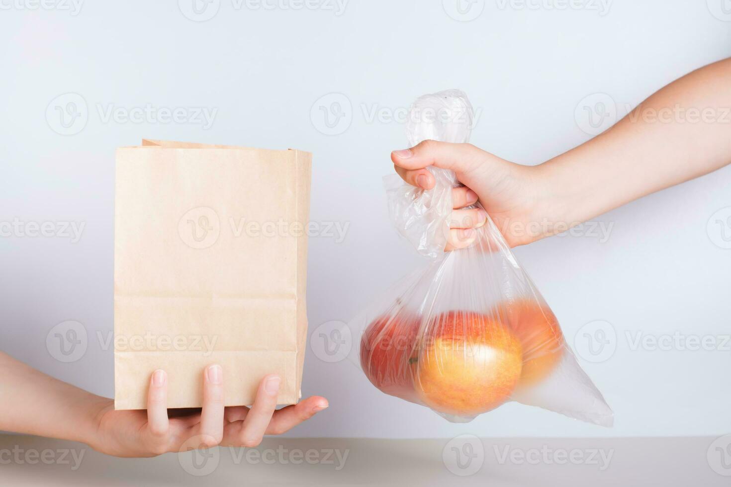 A hand with a disposable transparent bag of apples and a hand with an eco-friendly paper bag photo