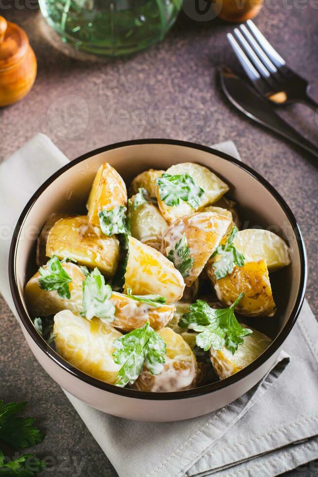 Delicious potato salad with parsley and mayonnaise in a plate on the table vertical view photo