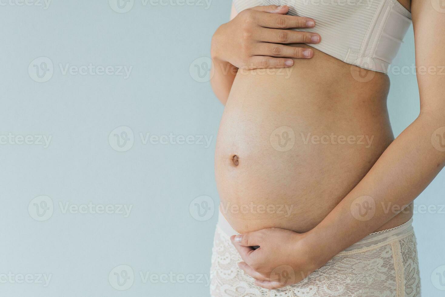 Pregnant woman holds hands on belly and pastel color background. Pregnancy, maternity, preparation and expectation concept. Close-up, copy space. Young woman waiting for baby birth. photo