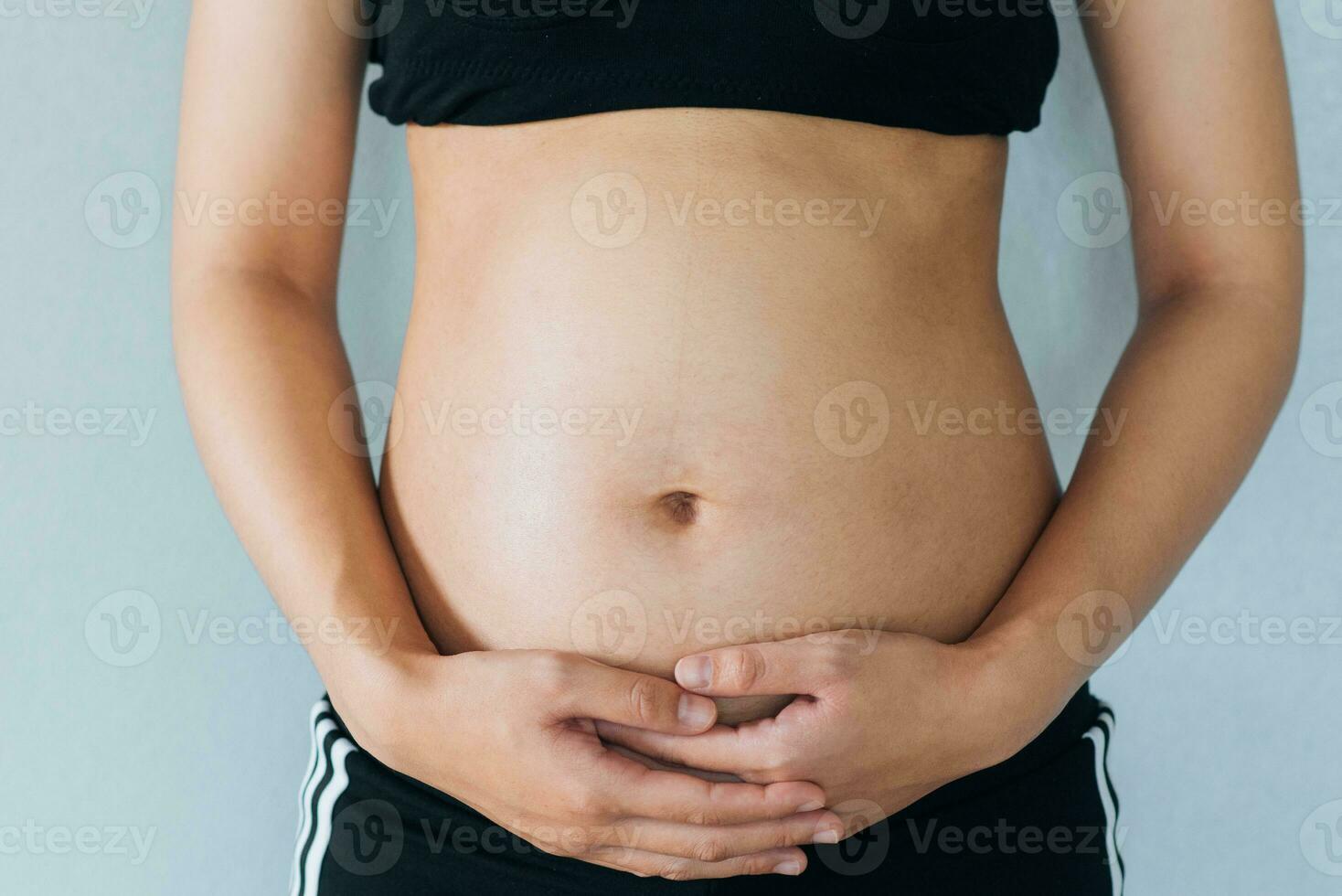 Pregnant woman holds hands on belly and pastel color background. Pregnancy, maternity, preparation and expectation concept. Close-up, copy space. Young woman waiting for baby birth. photo