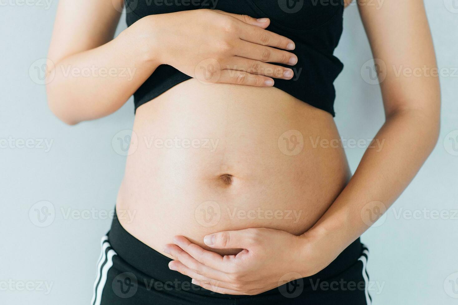 Pregnant woman holds hands on belly and pastel color background. Pregnancy, maternity, preparation and expectation concept. Close-up, copy space. Young woman waiting for baby birth. photo