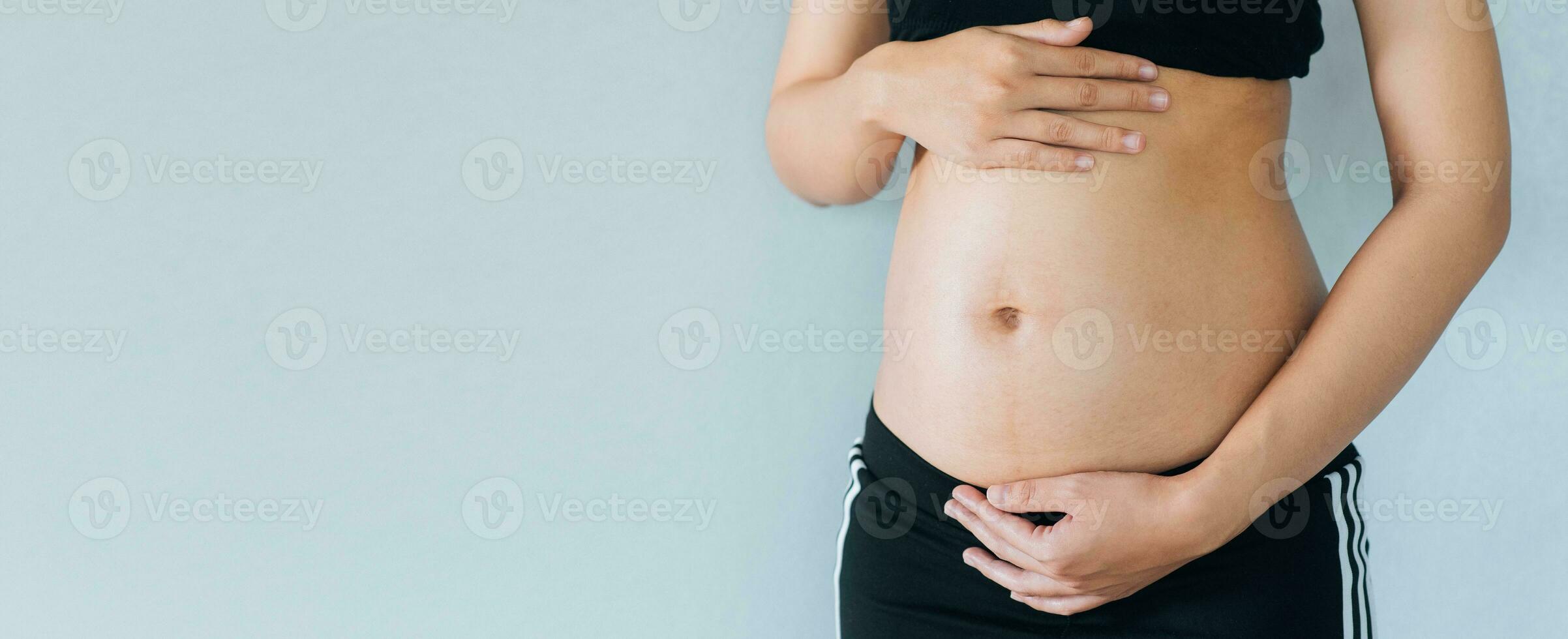 Pregnant woman holds hands on belly and pastel color background. Pregnancy, maternity, preparation and expectation concept. Close-up, copy space. Young woman waiting for baby birth. photo