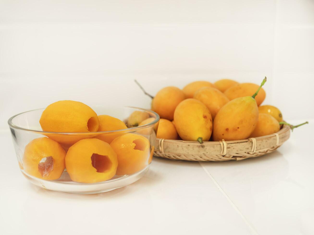 ripe juicy peeled marian plum or plum mango fruit serve in glass bowl and woven bamboo tray over white kitchen background, thailand fresh asian famous tropical fruit photo