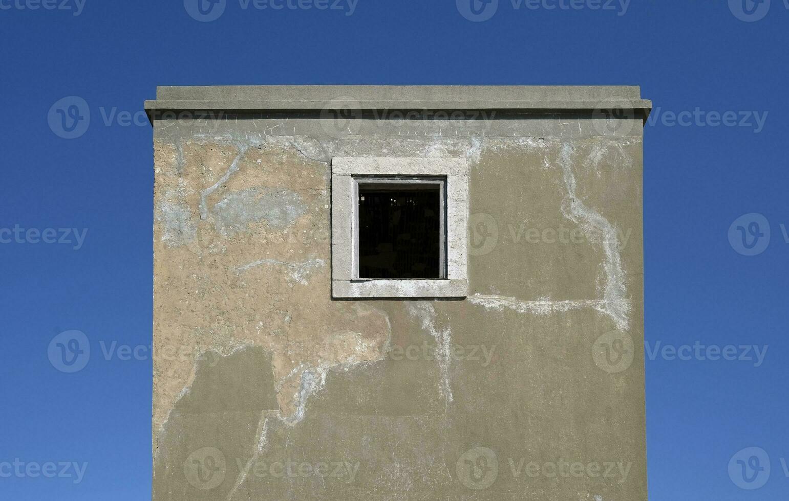 Symmetrical view of an abandoned building with a single window in the middle against a blue sky photo