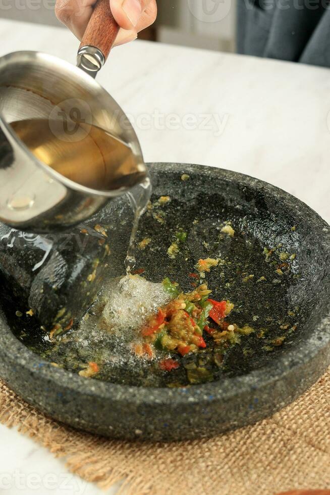 verter caliente petróleo a el mano de mortero con picante ajo y chile sambal foto