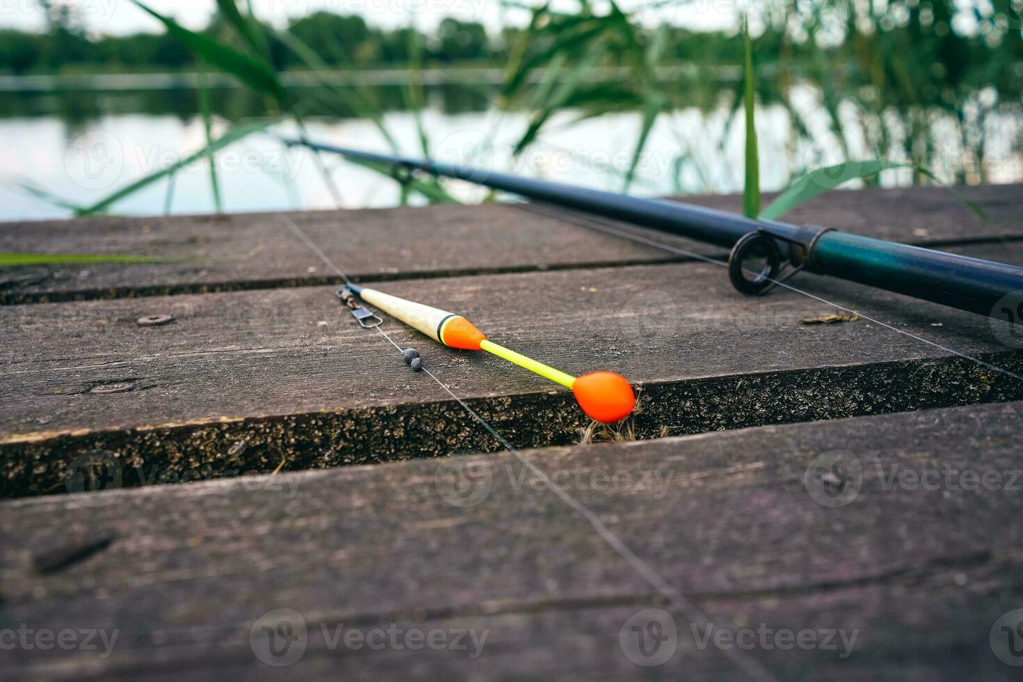 Fishing float, fishing bobber on the wooden pier. Fishing rod and fishing equipment on the jetty at the lake in the forest. Fishing concept. photo