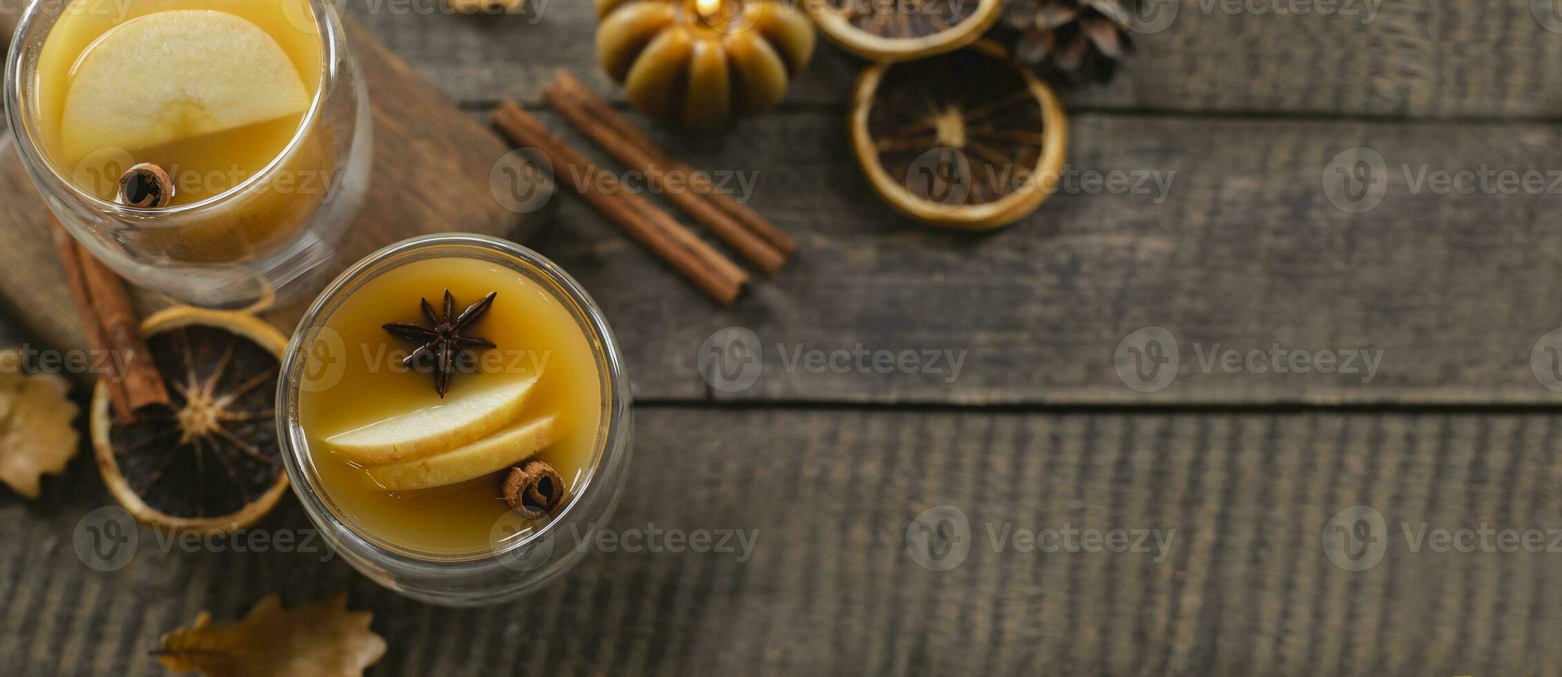 Autumn beverage in two glasses on wooden table background. Autumn warm cocktail with autumn fall leaves, cinnamon sticks and candle. Top view. Long Banner image for design photo