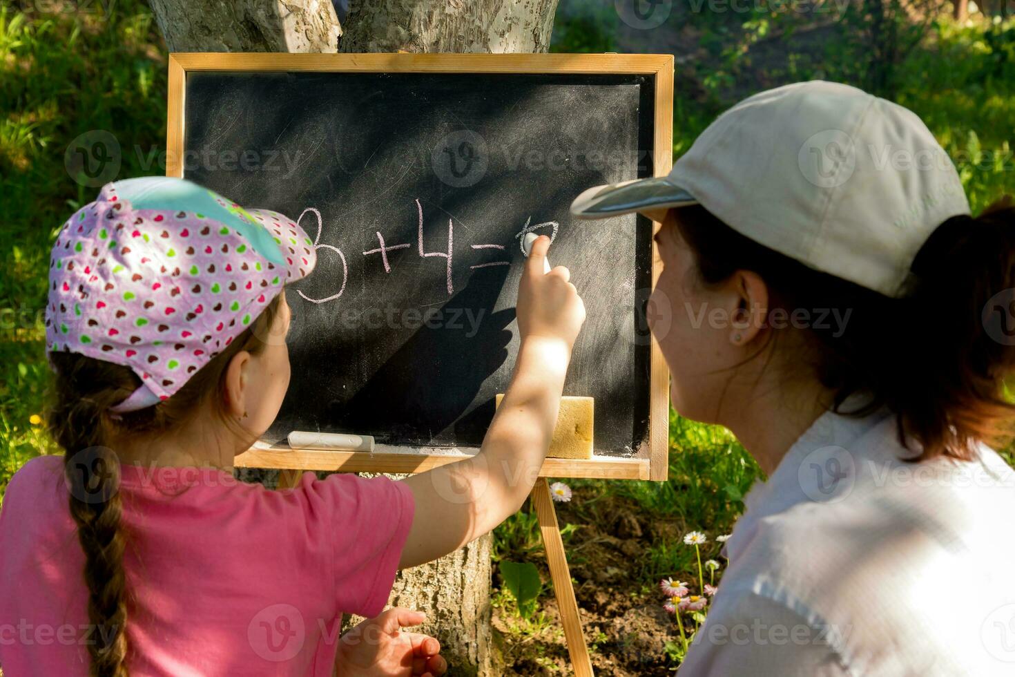 mom and daughter solve examples on a slate board in the garden in summer photo