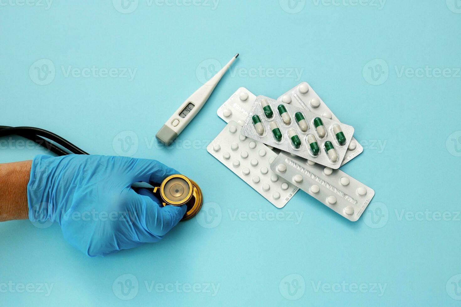 the hand of a medic holds a stethoscope, next to a thermometer and pills photo