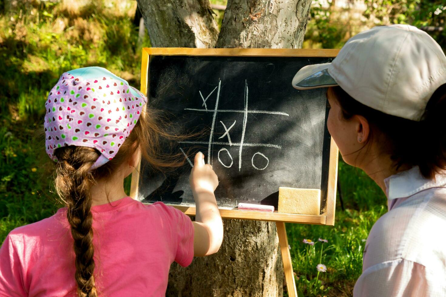 mother and daughter in the garden playing tic-tac-toe on a slate board. photo