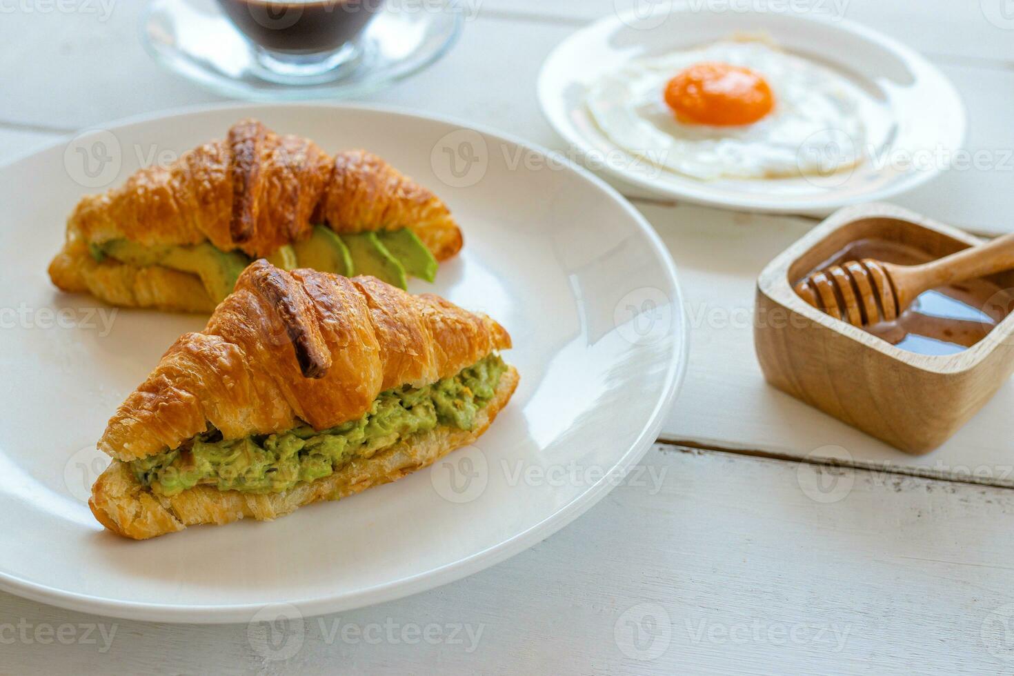 Croissant sandwich with egg,avocado on white dish and honey, coffee. breakfast and healthy food concept. photo