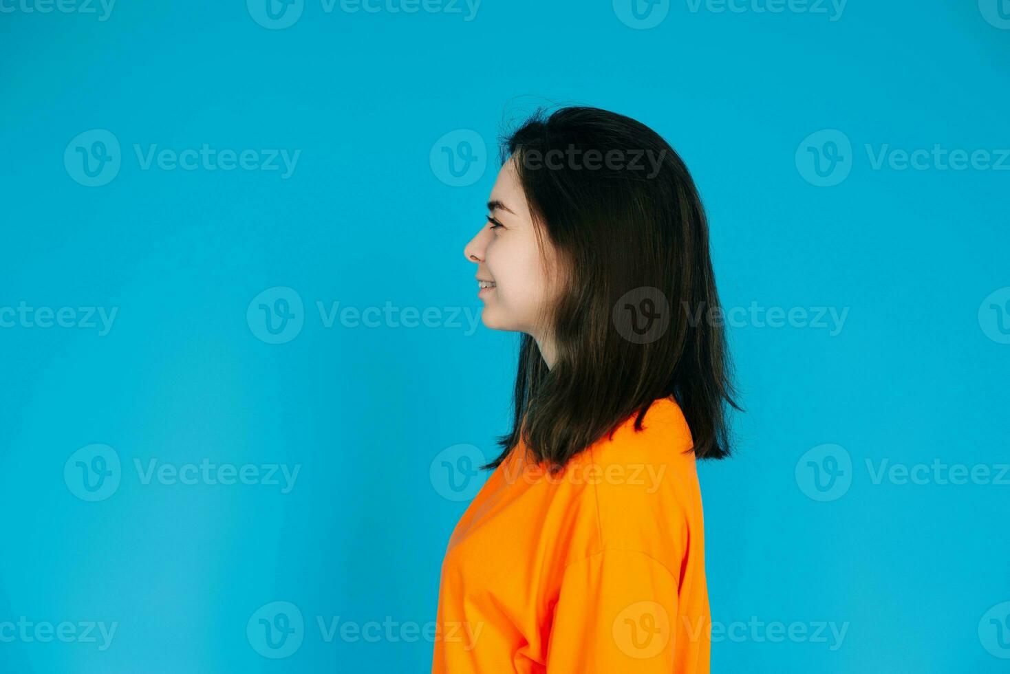 radiante joven mujer en elegante naranja atuendo sonriente con un radiante dentado sonrisa, perfil retrato, aislado en azul antecedentes foto