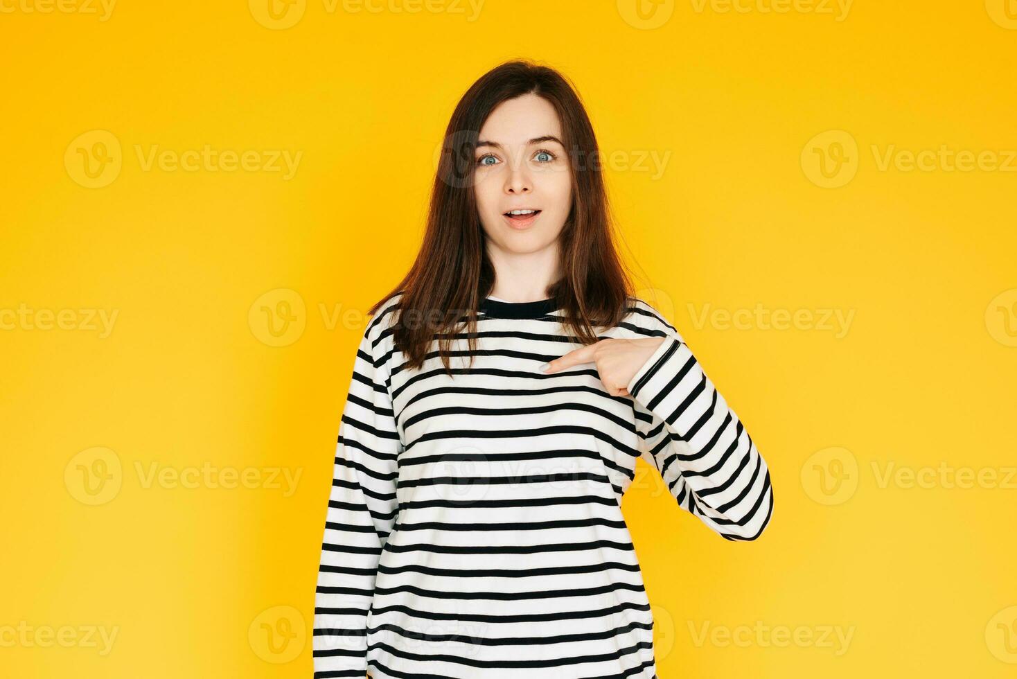 Delighted Woman Pointing at Herself in Amazement - Humorous Reaction Concept on Bright Yellow Background. Surprised and Amused Woman Pointing at Herself with Open Mouth - Self-Recognition Humor photo