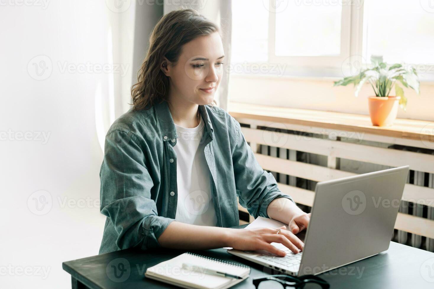 Young woman multitasking with a laptop in a modern office environment and student girl focused on work from home. Online work, study, freelance, business, and office lifestyle concept photo