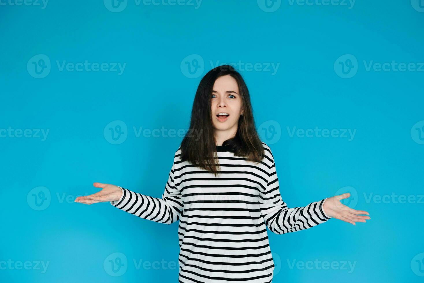 Captivating Portrait of Astonished Woman in Striped Pullover - Surprised and Amazed Female Model with Arms Extended - Isolated on Blue Background - Perfect for Expressing Shock, Surprise, and Emotion photo