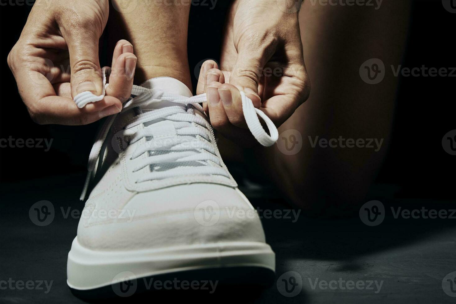 Woman hands tying shoelaces on sneakers on dark background. Fitness athlete ready for exercise photo