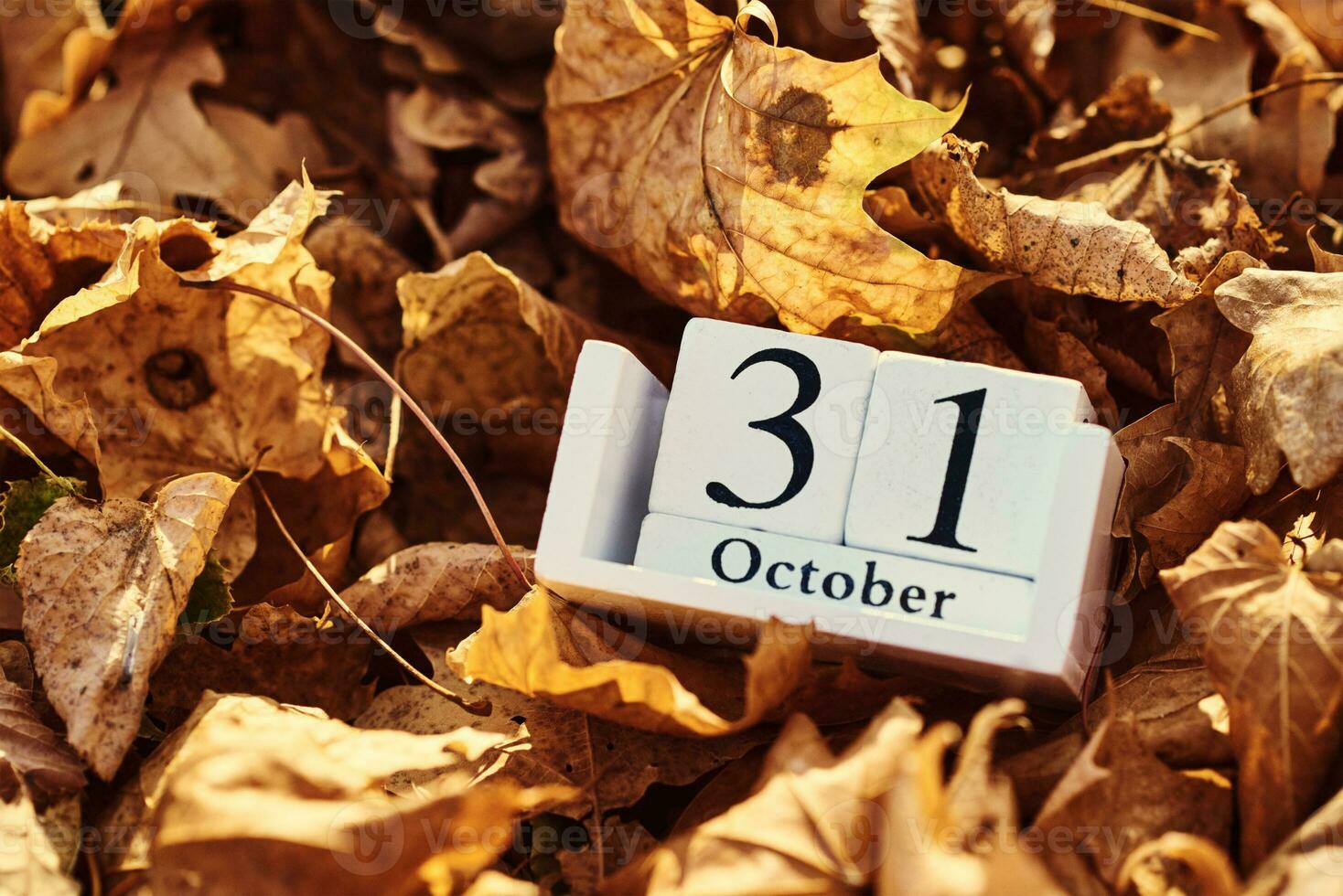 Wooden calendar block with date 31 october on a falling autumn leaves background photo