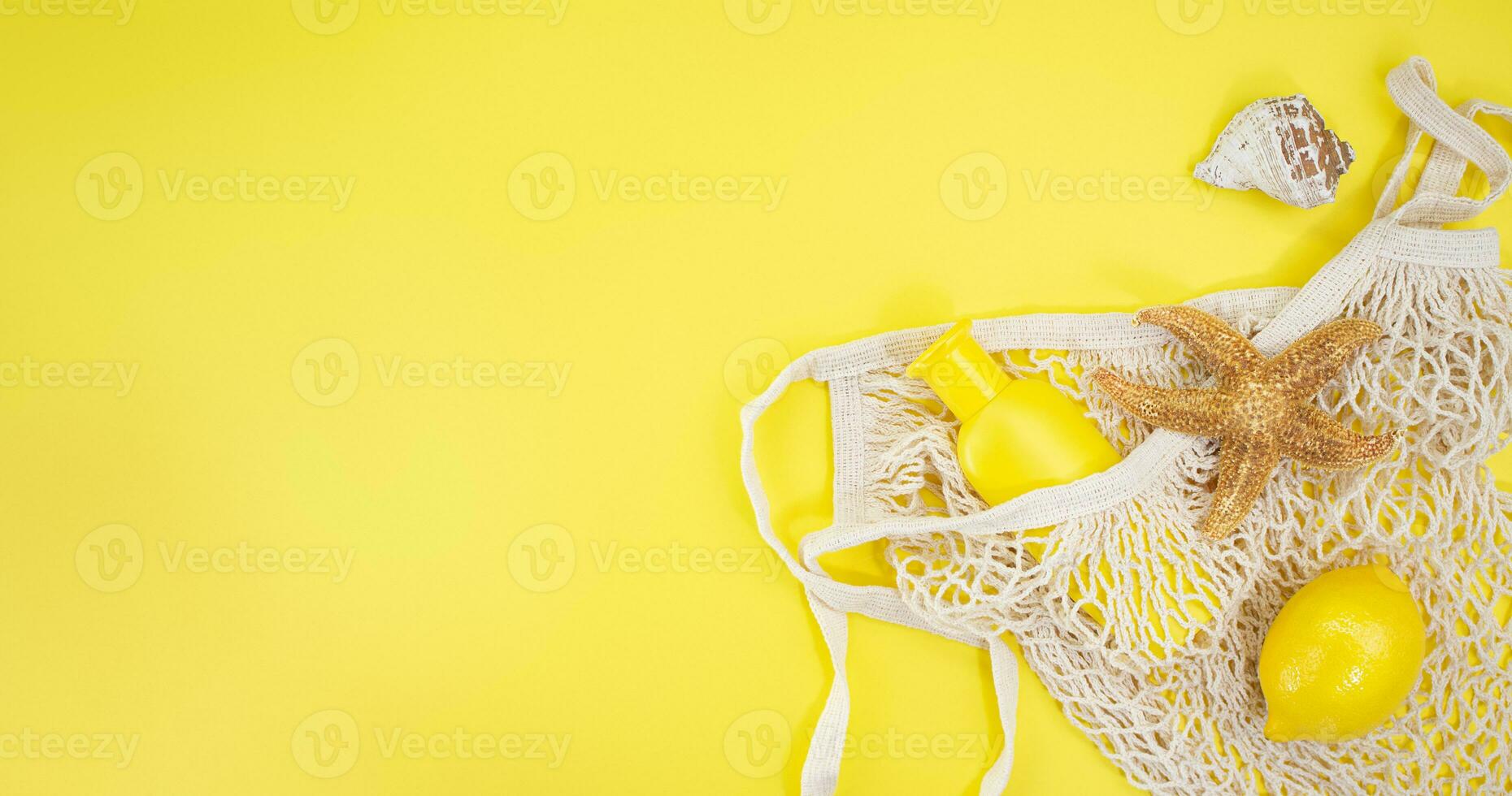 Starfish, shells with bag string with sunscreen bottle mockup and lemon from the side on yellow background. Concept of summer time, vacation, travel. Banner. Copy space photo