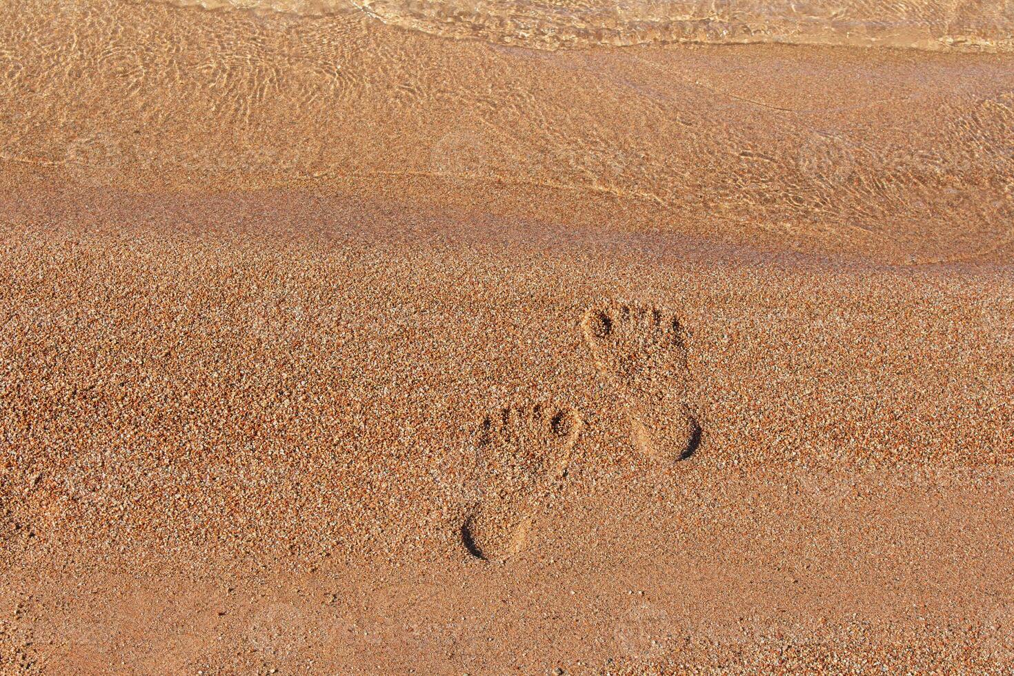 Human footprints on sand of beach near sea coast. Monochrome. Vacation, travel, summer. Steps on shore. Copy space photo