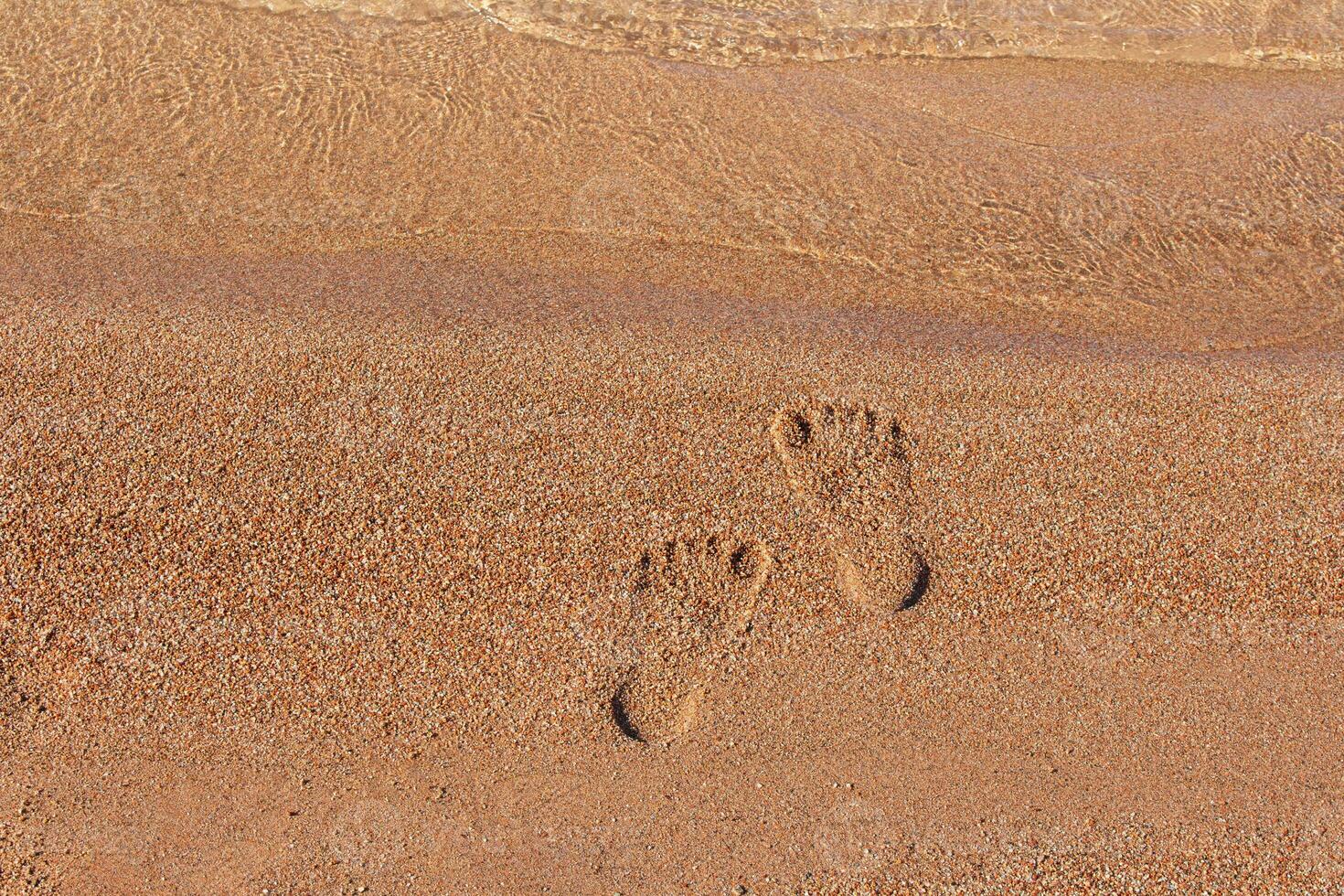 Human footprints on sand of beach near sea coast. Monochrome. Vacation, travel, summer. Steps on shore. Copy space photo