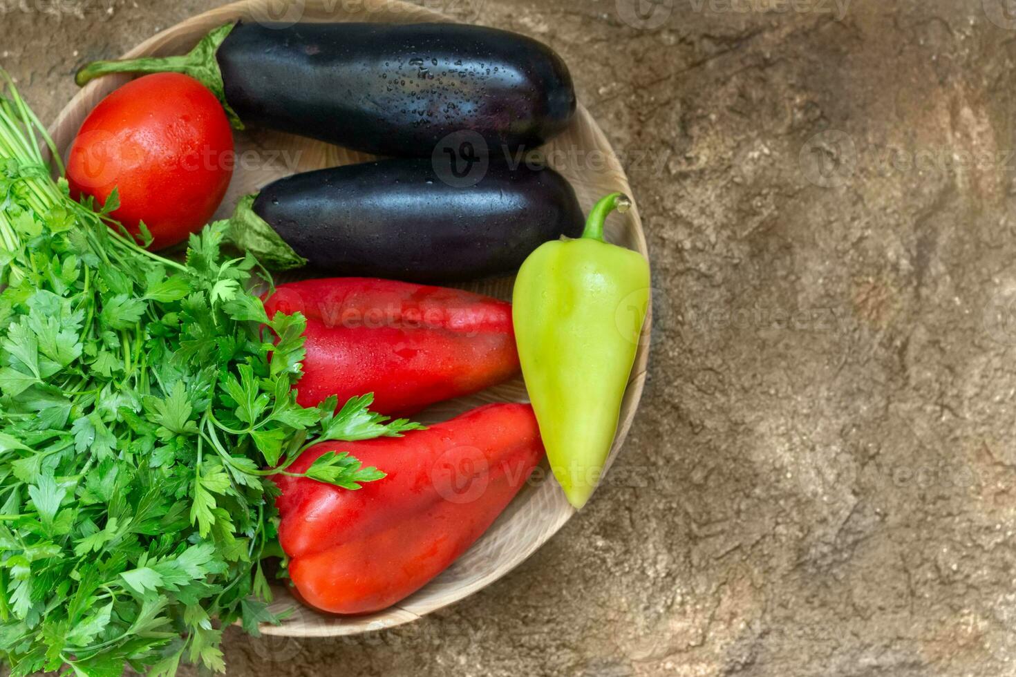 Red tomato, pepper, parsley, eggplant lie on a wooden plate on a brown background. Ingredient for cooking. view from above. Copy space photo