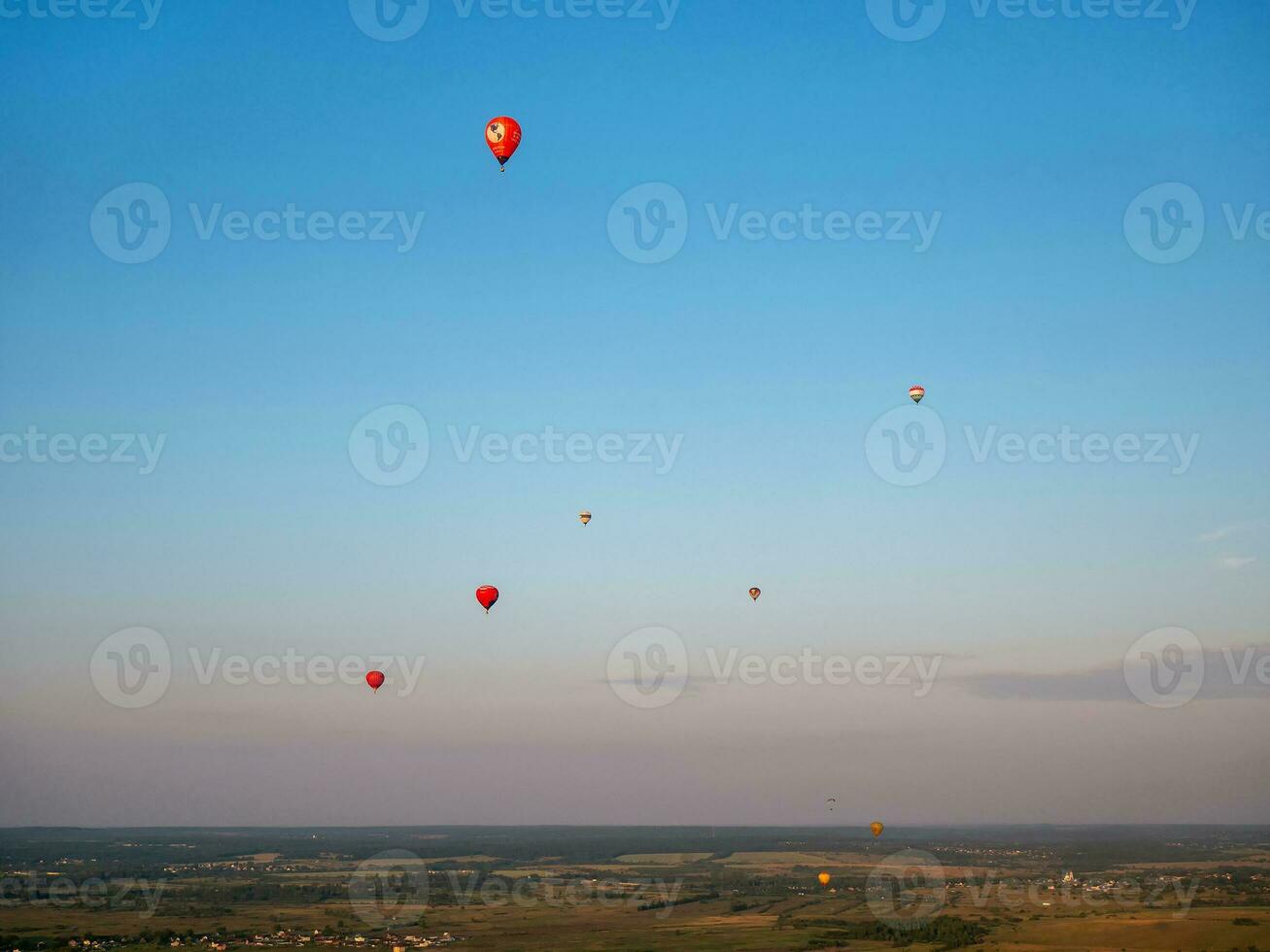 Colorful air balloon is flying in free flight over the field. Bird's-eye view. Multicolored balloon in the sky at sunset photo