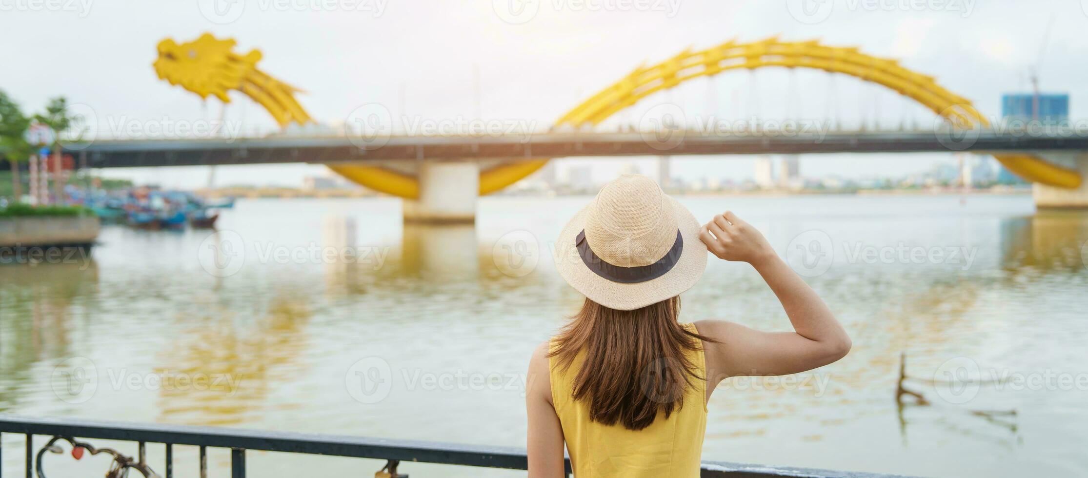 Woman Traveler with yellow dress visiting in Da Nang. Tourist sightseeing the river view with Dragon bridge at love lock bridge. Landmark and popular. Vietnam and Southeast Asia travel concept photo