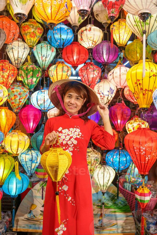 contento mujer vistiendo ao dai vietnamita vestir con vistoso linternas, viajero Turismo a hoi un antiguo pueblo en central vietnam.punto de referencia para turista atracciones.vietnam y Sureste viaje concepto foto