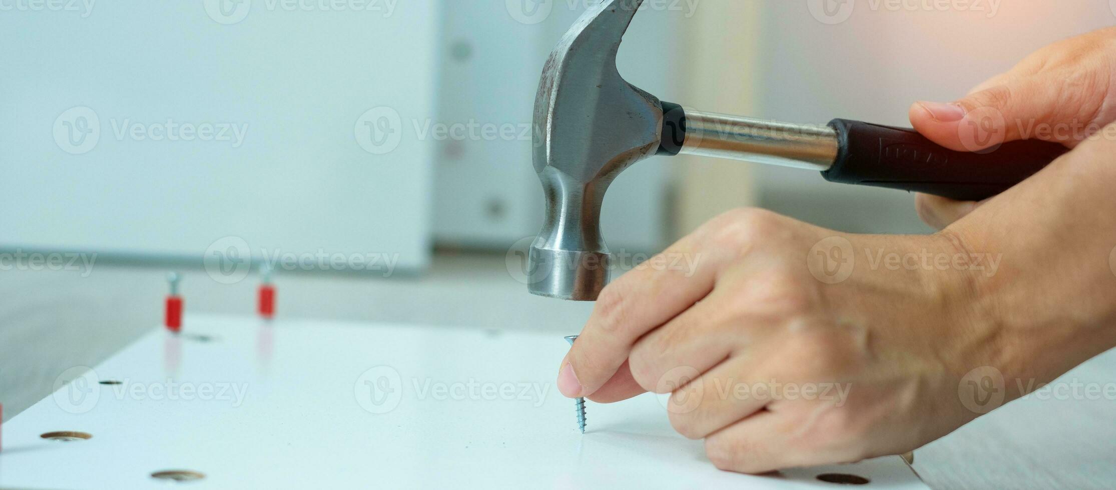 man using hammer hammering a nail into wooden boards, assembling or repairing furniture at home. DIY, Renovation, repairing and development home or apartment concepts photo