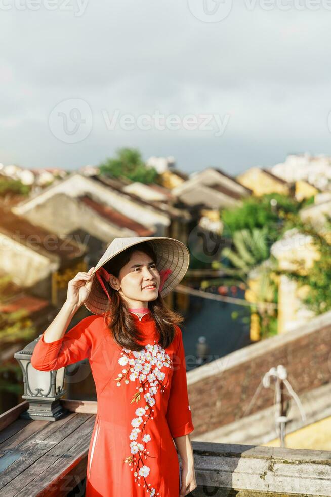 happy woman wearing Ao Dai Vietnamese dress, traveler sightseeing view at rooftop in Hoi An ancient town. landmark and popular for tourist attractions. Vietnam and Southeast travel concept photo