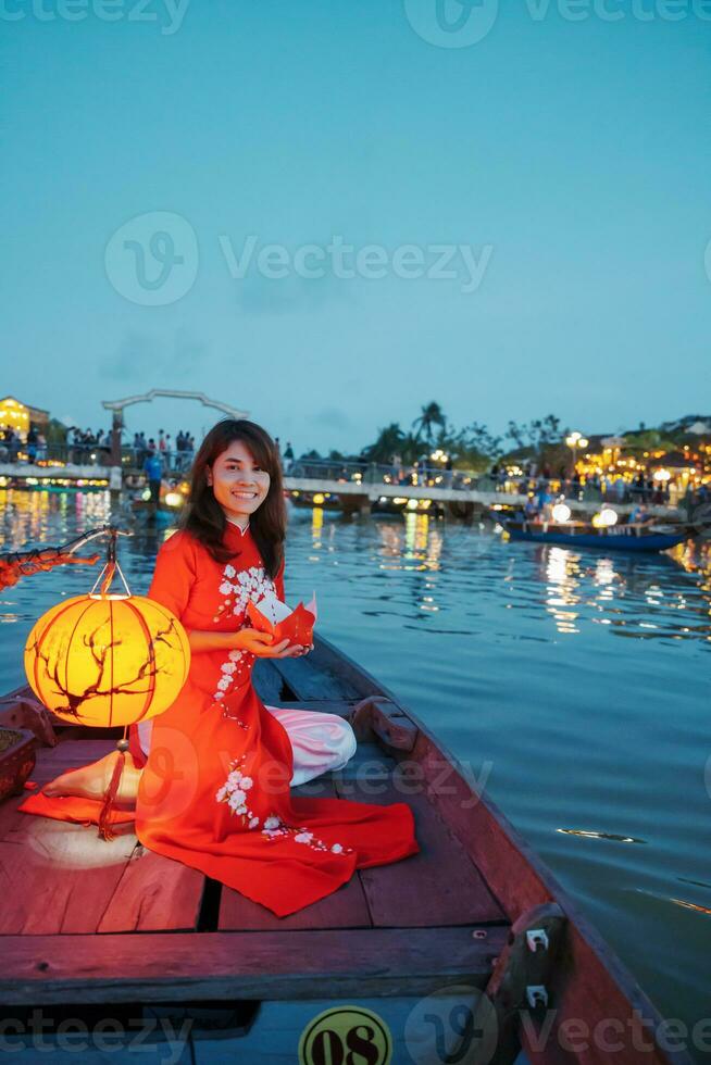 woman wearing Ao Dai Vietnamese dress, traveler Sightseeing Boat Ride and floating paper lantern at Hoi An ancient town. landmark for tourist attractions.Vietnam and Southeast travel concept photo