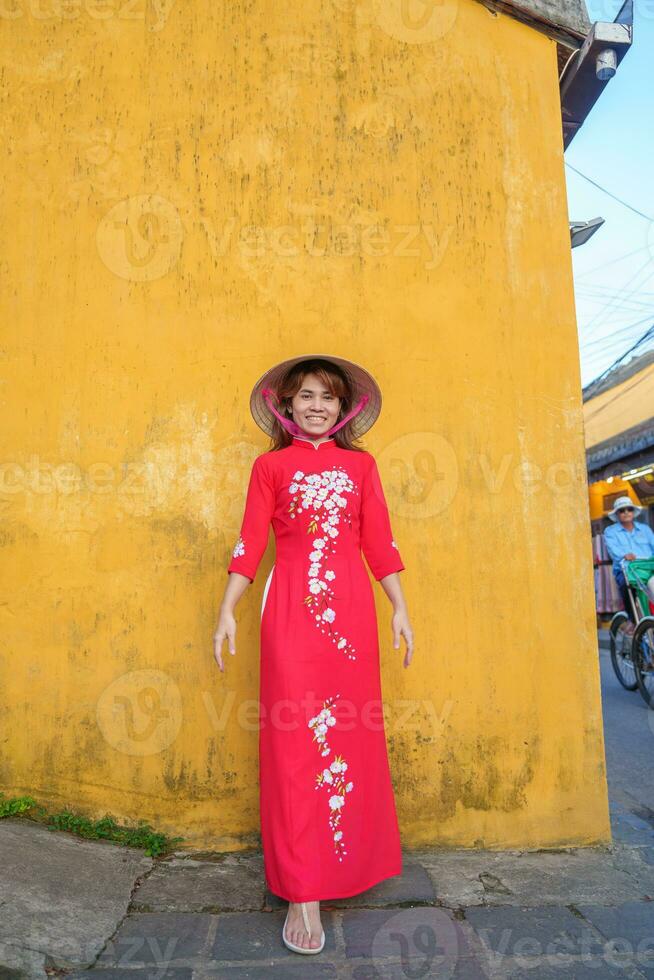 happy woman wearing Ao Dai Vietnamese dress and hat, traveler sightseeing at Hoi An ancient town in central Vietnam. landmark and popular for tourist attractions. Vietnam and Southeast travel concept photo