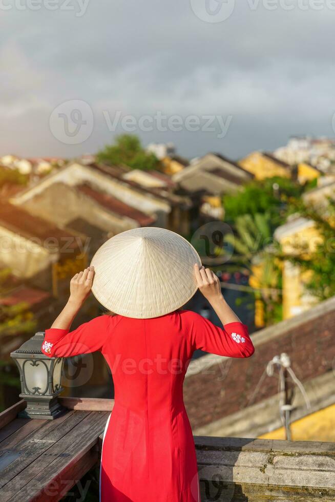 happy woman wearing Ao Dai Vietnamese dress, traveler sightseeing view at rooftop at Hoi An ancient town in Vietnam. landmark and popular for tourist attractions. Vietnam and Southeast travel concept photo
