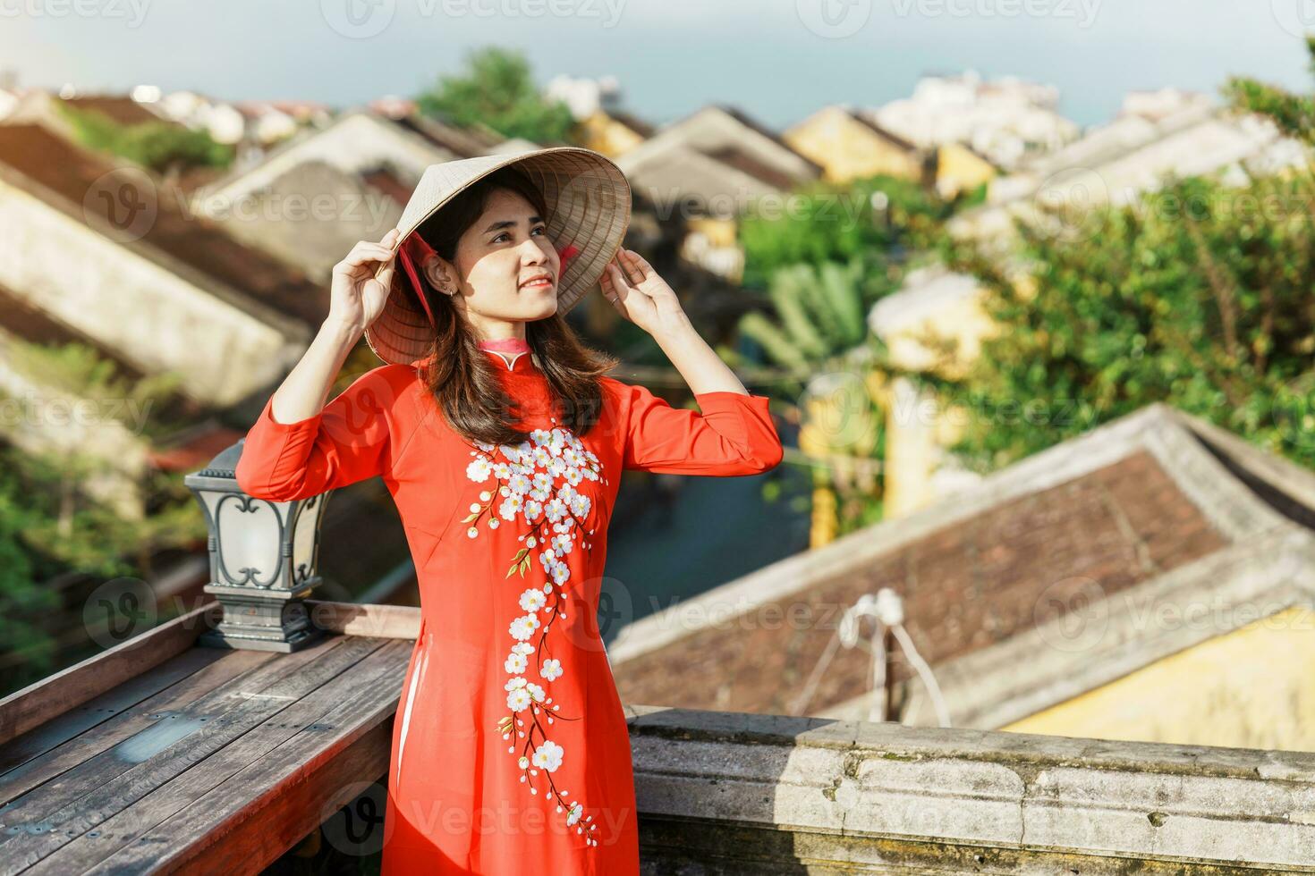 happy woman wearing Ao Dai Vietnamese dress, traveler sightseeing view at rooftop at Hoi An ancient town in Vietnam. landmark and popular for tourist attractions. Vietnam and Southeast travel concept photo