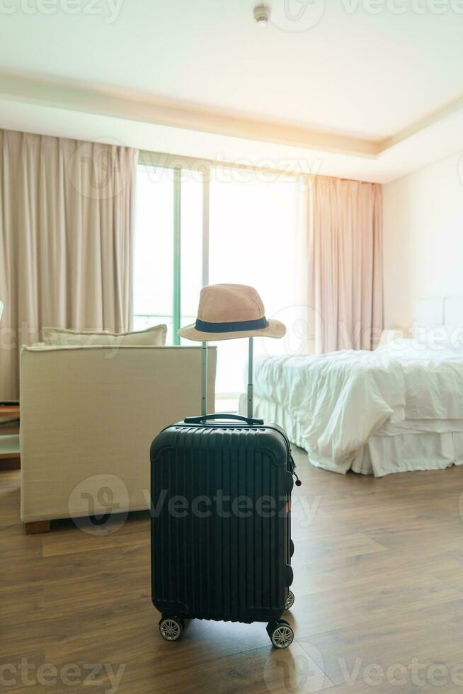 Black Luggage with hat in modern hotel room after door opening. Baggage for Time to travel, service, journey, trip, summer holiday and vacation concepts photo